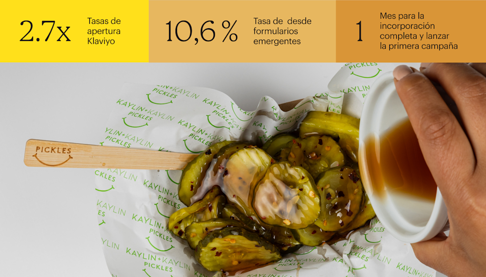 Tiras de pepinillo rociadas con salsa blanca sobre un papel de la marca con el patrón del logotipo de cara sonriente verde y un tenedor de madera